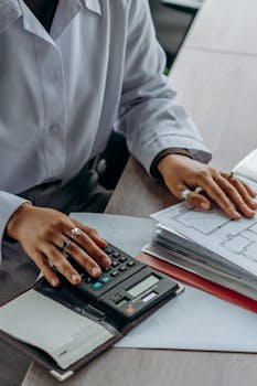 A Person Working on the Documents Using a Calculator