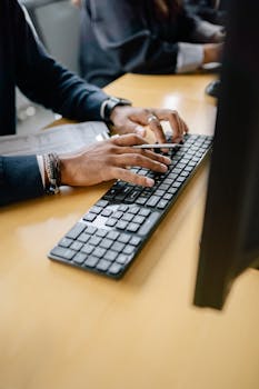 Person Holding a Pencil While Typing on the Black Keyboard